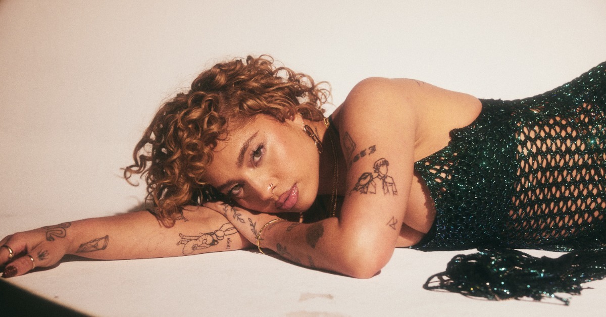 Kiana Ledé tattoos: Reclining portrait showing fine-line arm tattoos