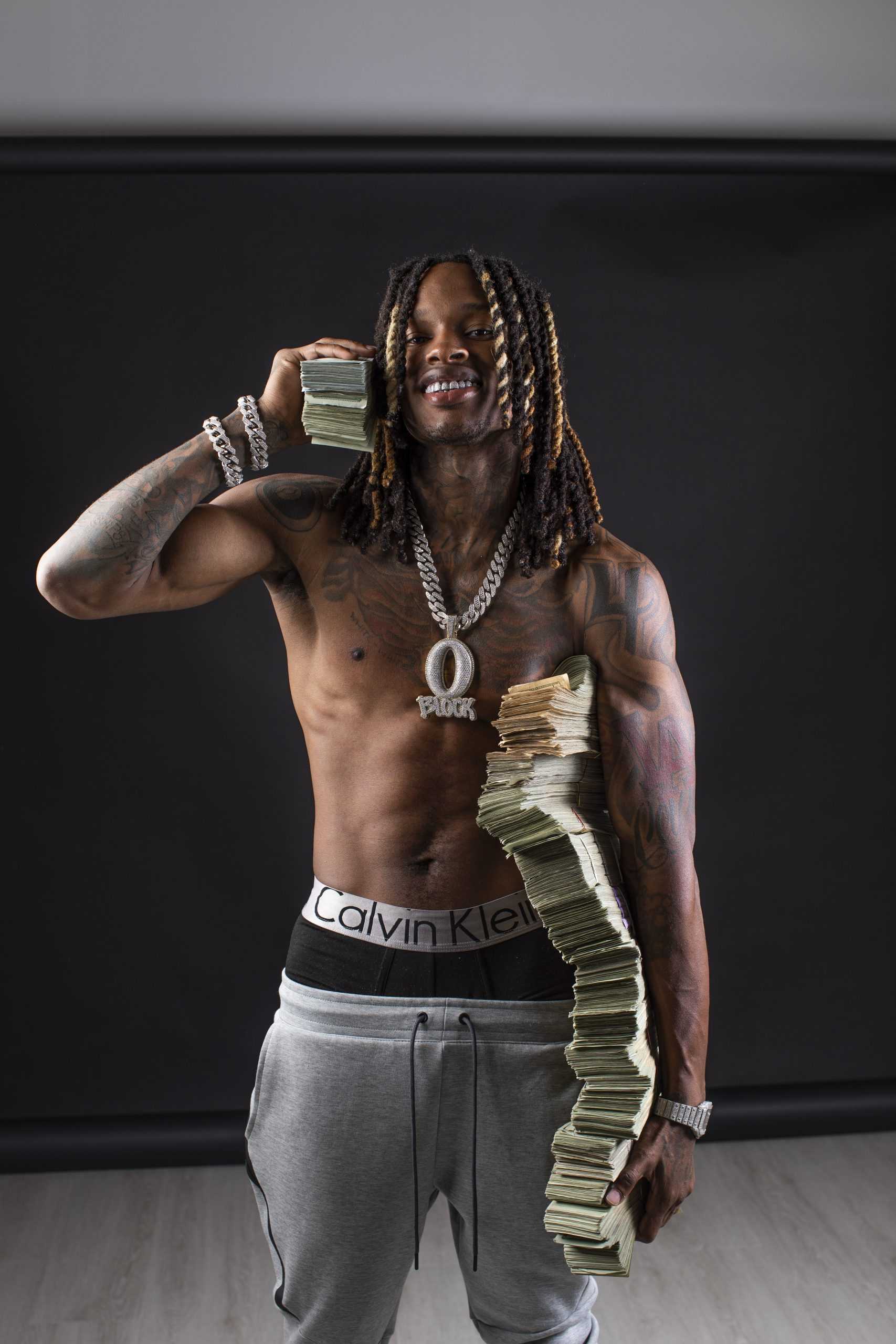 King Von tattoos: high-resolution angled portrait showing the wrapped arm work, chest tattoos and hand placement