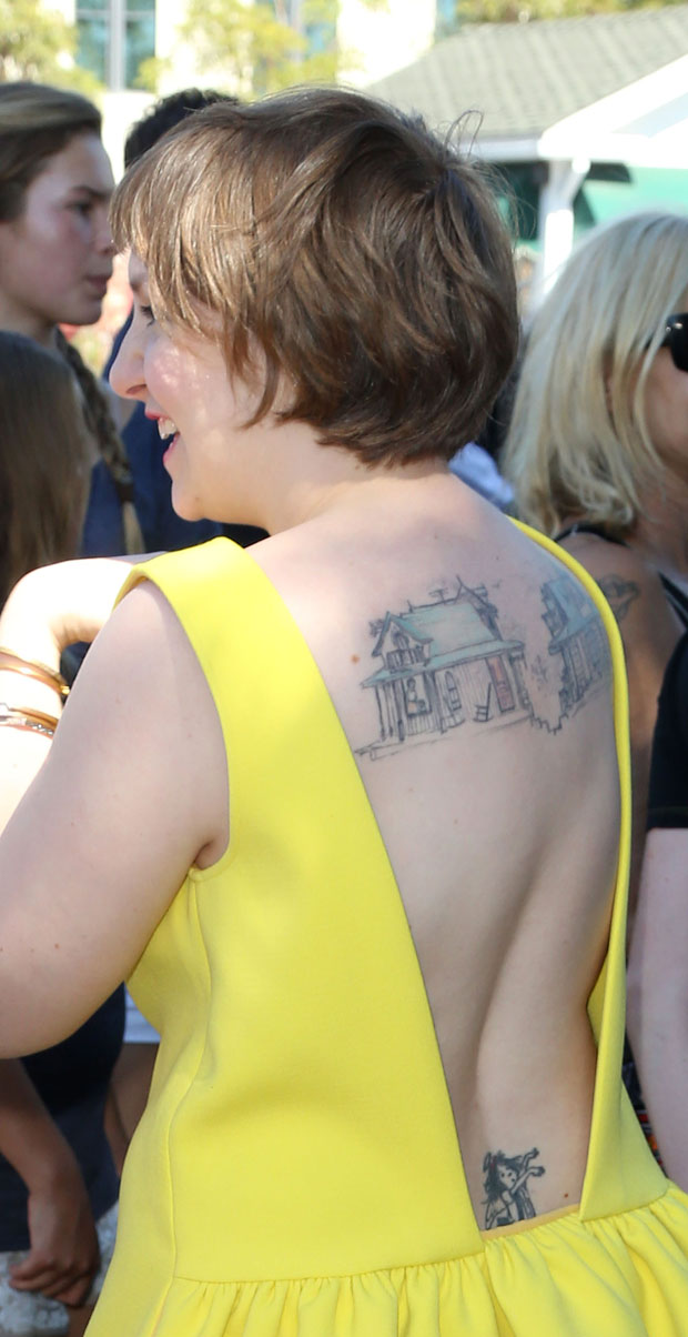 Lena Dunham tattoos: red-carpet back view showing the two architectural house tattoos across the upper back and the lower-back figure