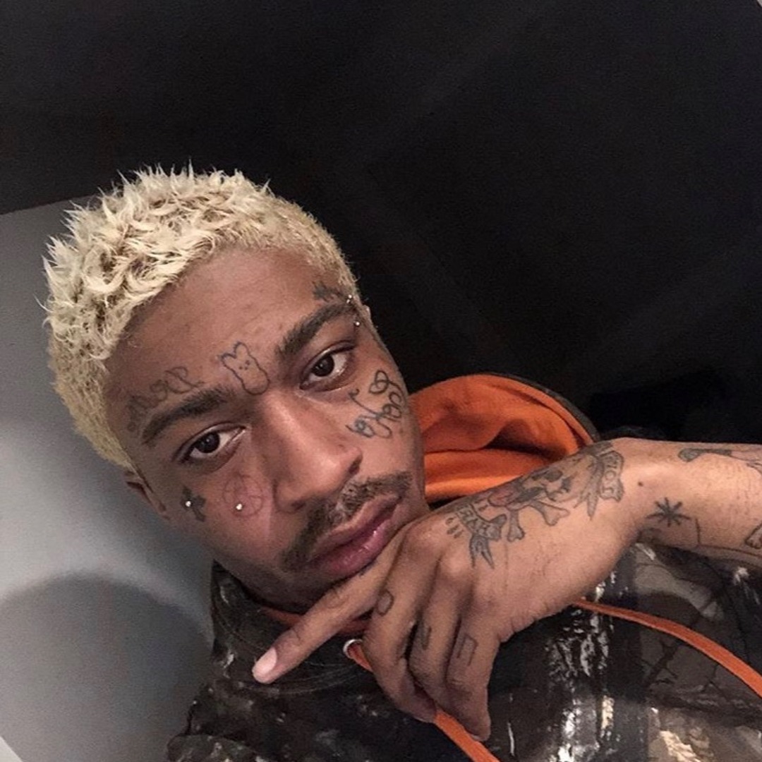 Lil Tracy tattoos: face symbols, cheek lettering, neck ink and arm tattoos in a close portrait