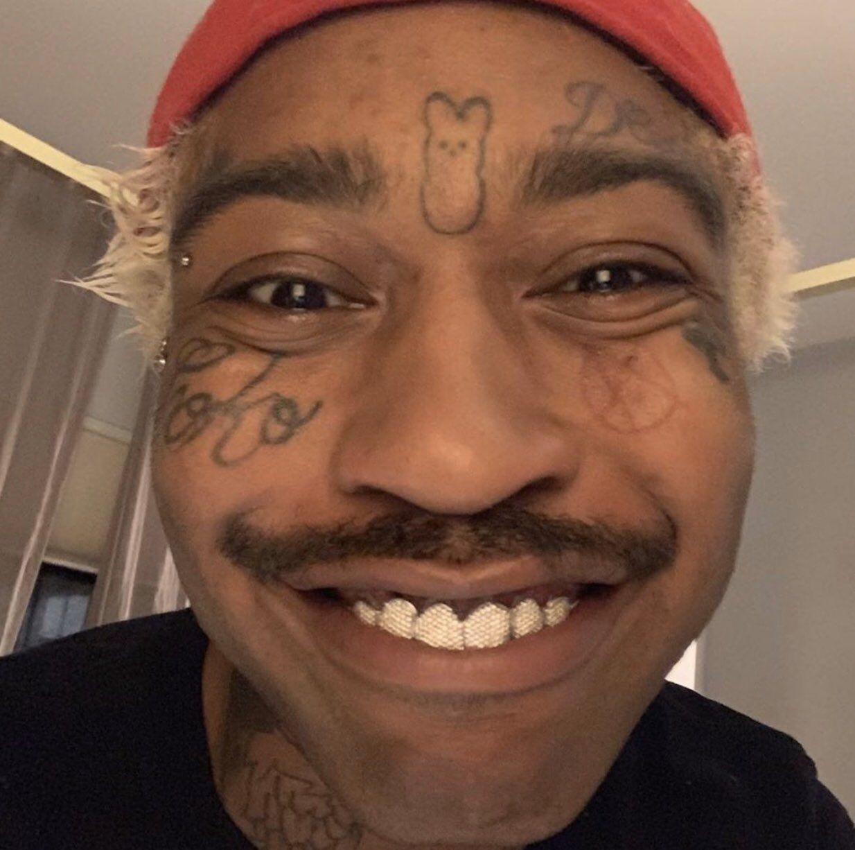 Lil Tracy tattoos: a clear forehead symbol, cheek script, eye marks and tattooed forearm