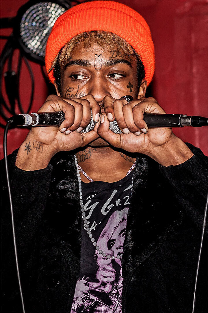 Lil Tracy tattoos: face, hand and wrist tattoos visible while holding two microphones