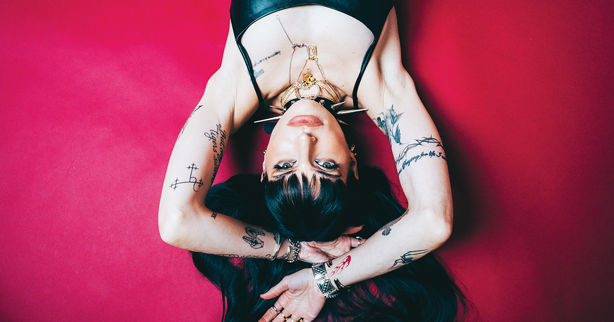 Lilith Czar tattoos: high-resolution Inked portrait with both forearms, script and symbols visible against a red background