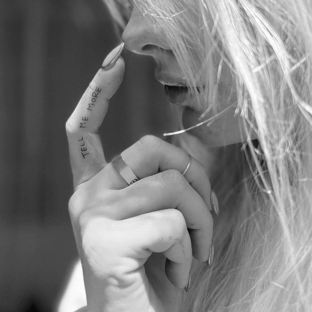 Madelyn Cline tattoos: Close tattoo photograph showing Madelyn Cline's vertical Tell Me More finger lettering.