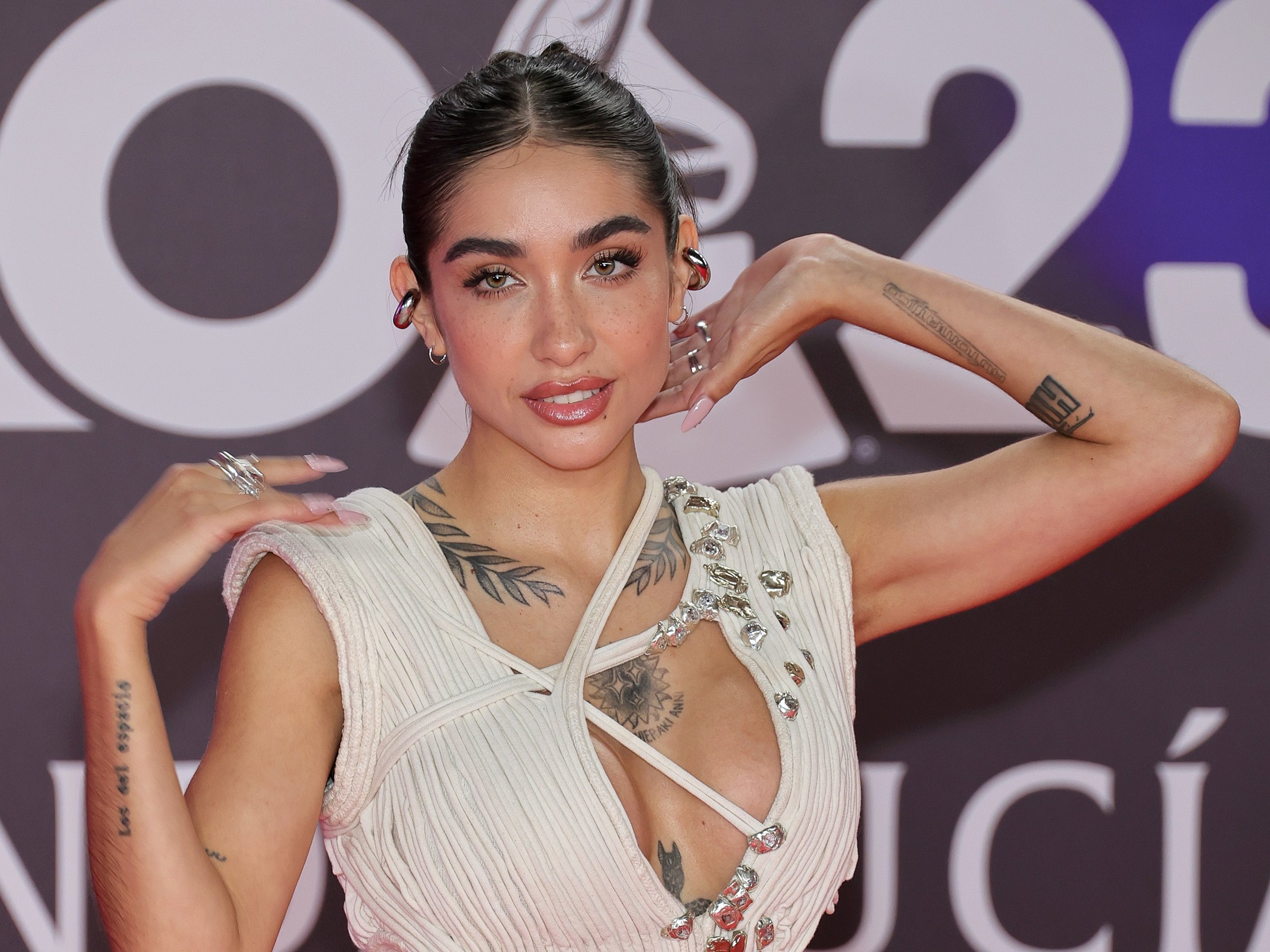 María Becerra tattoos: event portrait showing the readable Los del Espacio forearm lettering and chest coverage