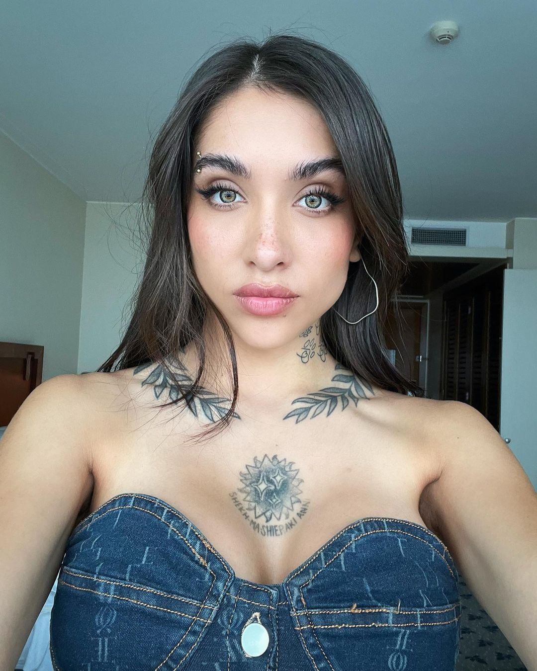 María Becerra tattoos: front portrait clearly showing the paired leaf branches and central chest emblem