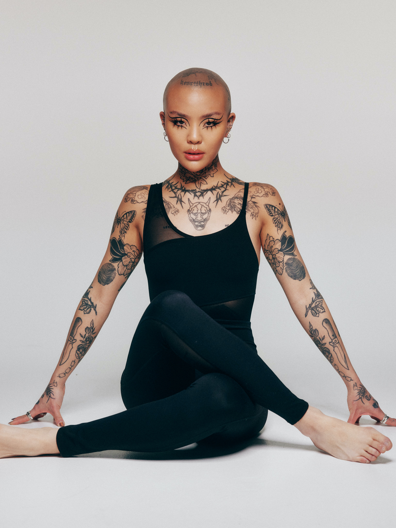 Mei Pang tattoos: full seated portrait showing paired arm, hand and leg tattoo coverage