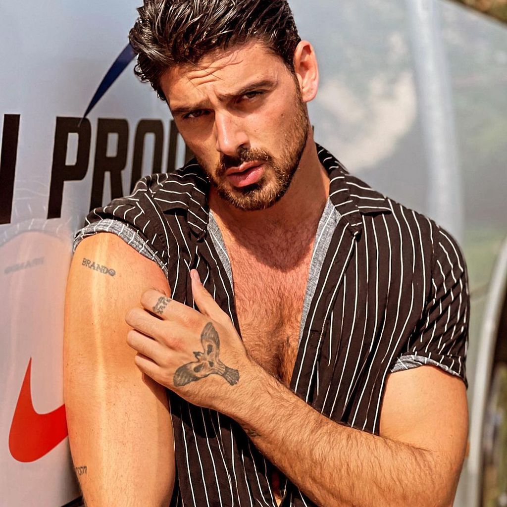Michele Morrone tattoos: The Brando lettering is visible on the upper arm, with hand ink also in frame.