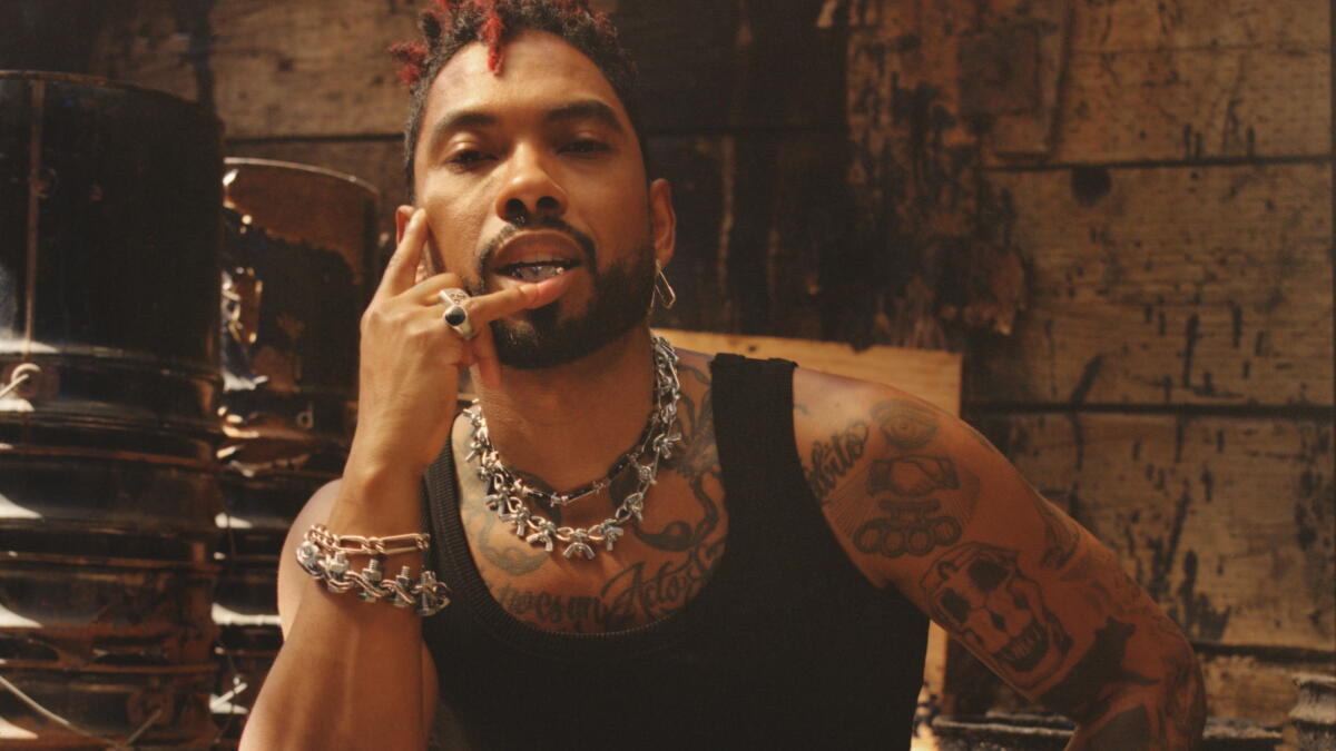 Miguel tattoos: arm and chest tattoos in a candid black tank top portrait