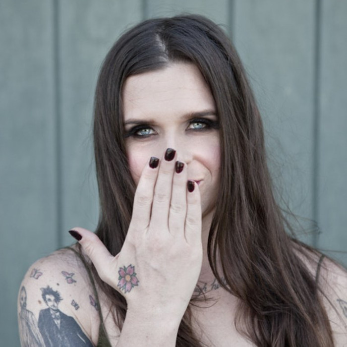 Mina Caputo tattoos: The AudioDB portrait provides a close view of the flower on the hand and the larger figure on the upper arm.