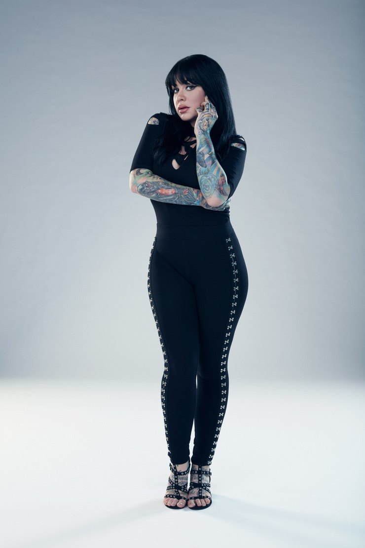 Nikki Simpson tattoos: face-visible portrait with both hands and colourful sleeve details visible against a clean background