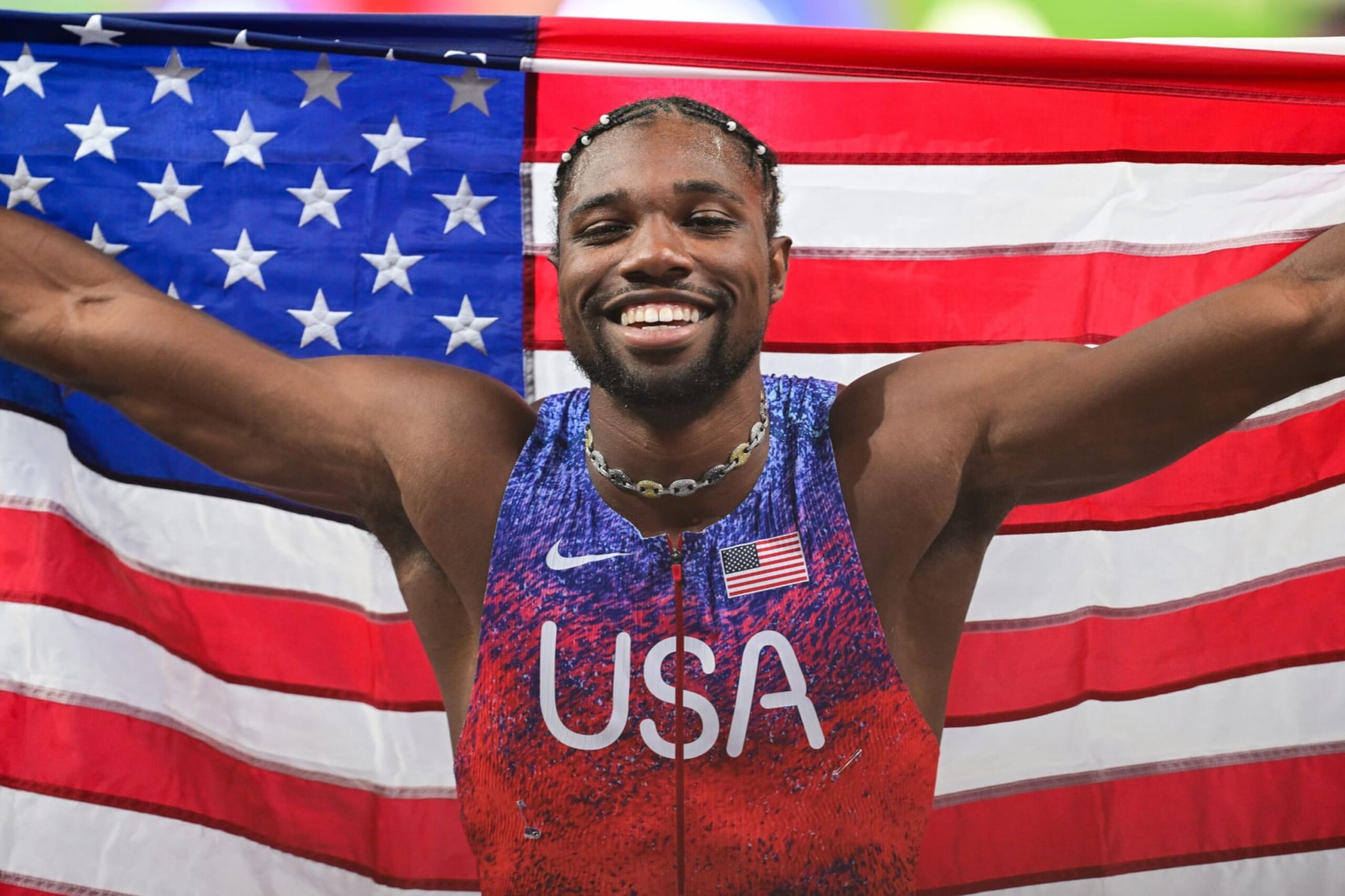 Noah Lyles in a contextual photograph: Contextual victory photograph of Lyles celebrating in front of the US flag; it does not show tattoo evidence.; not tattoo evidence