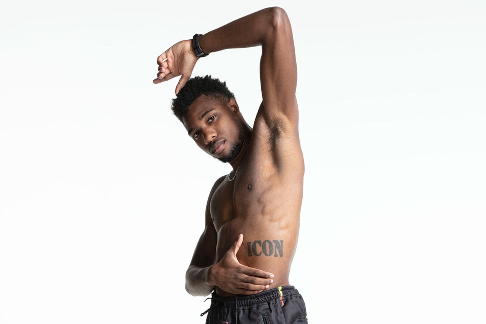 Noah Lyles tattoos: Clear first view of the uppercase ICON lettering across Lyles's torso, supporting the tattoo's placement and simple typography.