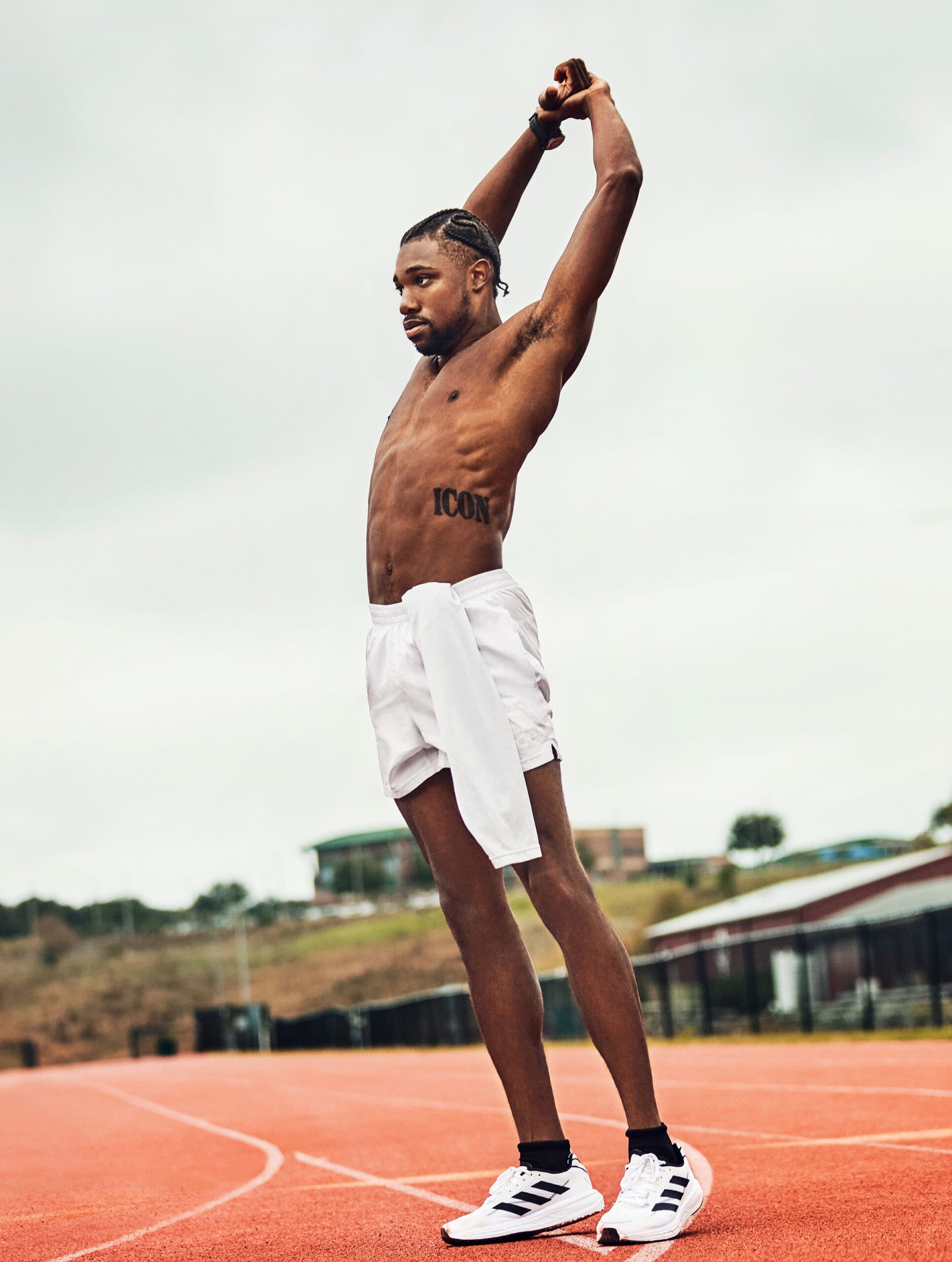 Noah Lyles tattoos: Distinct full-body stretch photograph with Lyles's face and the ICON lettering visible, providing a second genuine view of the same design.
