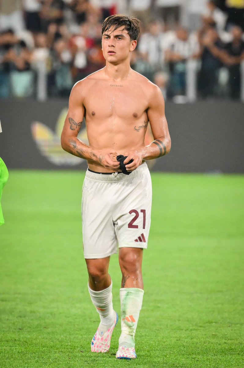 Paulo Dybala tattoos: full shirtless torso view showing the chest word, Arabic side lettering, arms and forearm bands