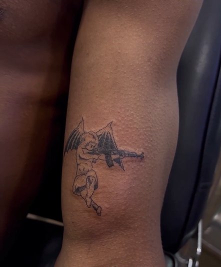 Rema tattoos: inline angel bat wings and gun bicep tattoo image