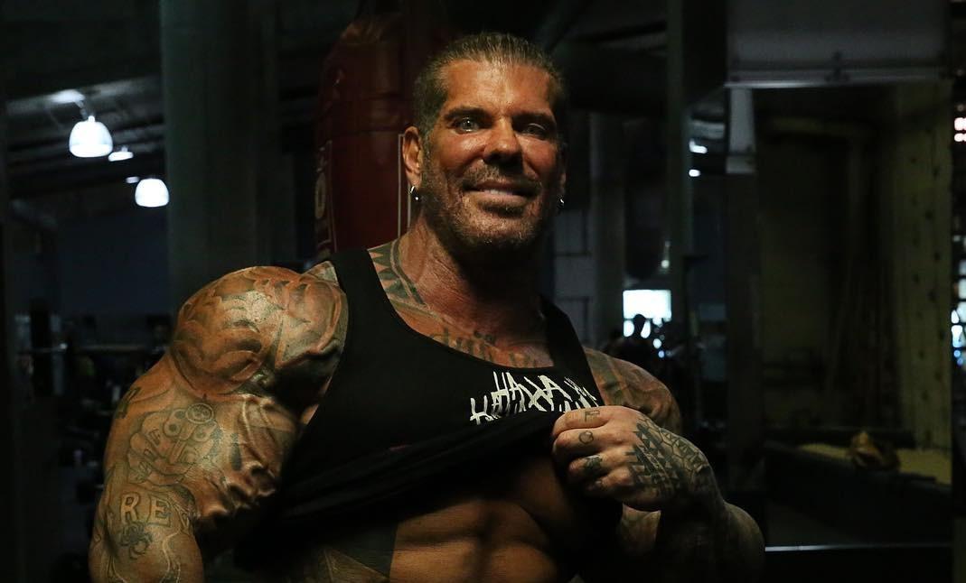 Rich Piana tattoos: clear face-visible wider gym photograph showing the overall black-and-grey balance across the arms and chest
