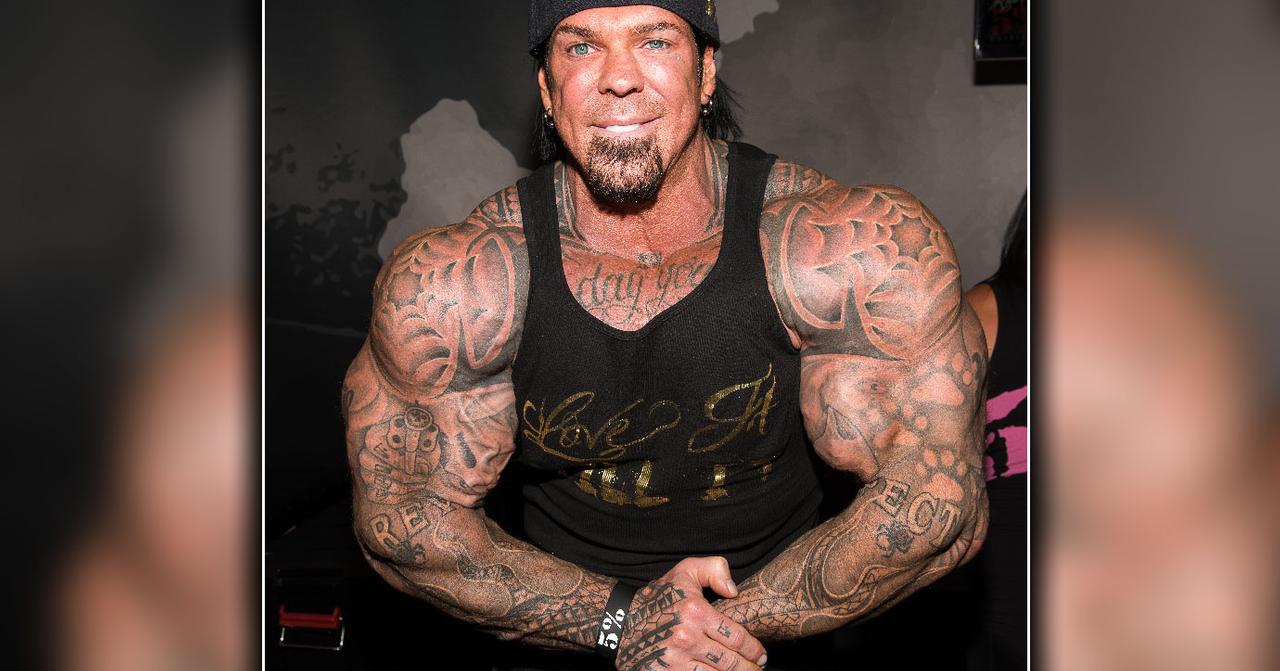 Rich Piana tattoos: face-visible gym photograph showing chest script connected to darker shoulder and upper-body work