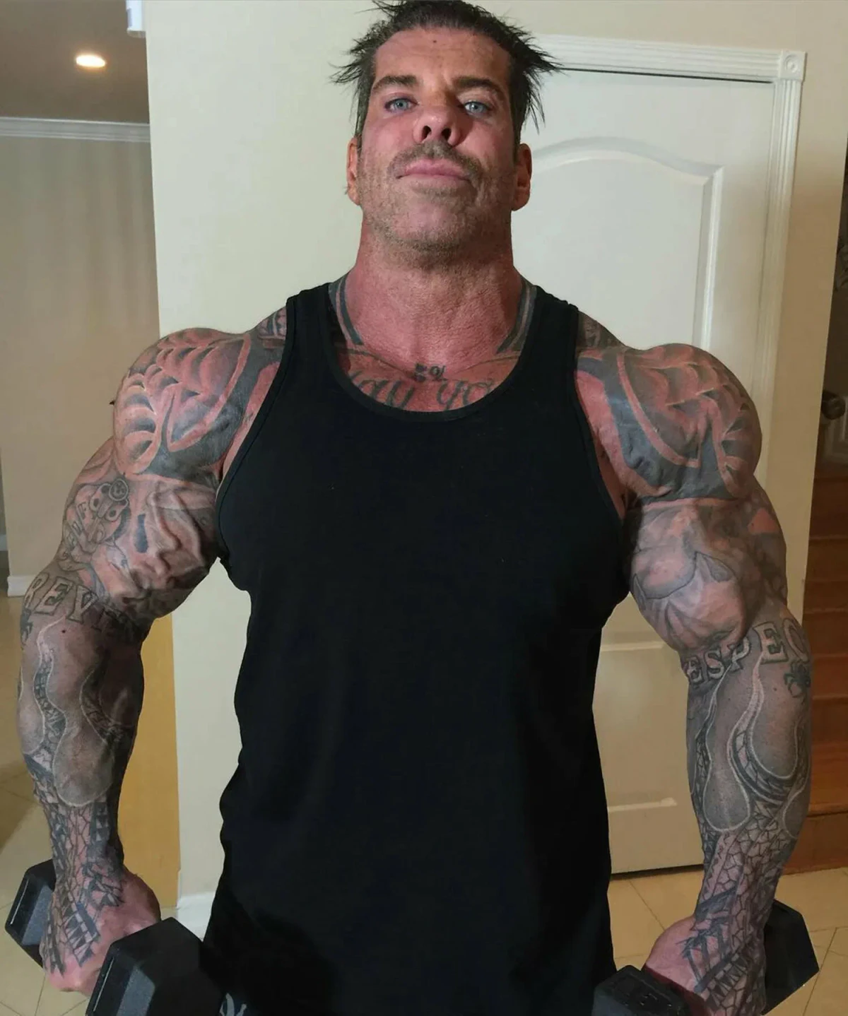 Rich Piana tattoos: face-visible gym portrait showing the smaller hand and wrist marks beside the larger arm collection