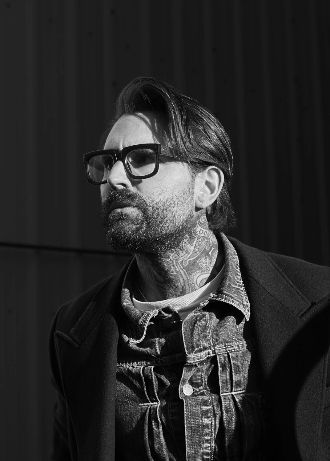 Ricki Hall tattoos: sharp portrait focused on the layered neck work and the way lettering and ornamental marks wrap around the throat