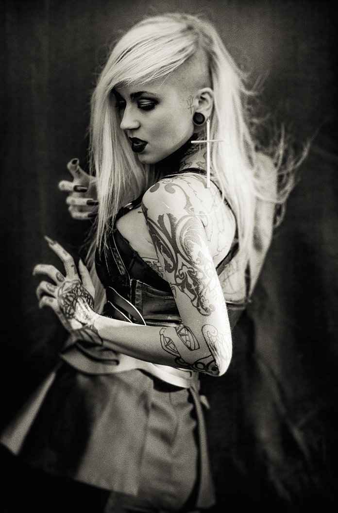 Sara Fabel tattoos: Bold upper arm creature forms and outlined forearm objects clearly distinguishable.
