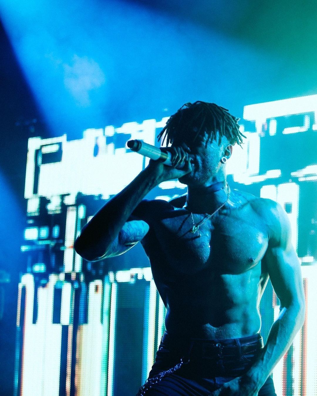 Scarlxrd tattoos: high-resolution concert photograph showing tattooed chest, arms and neck under blue stage light