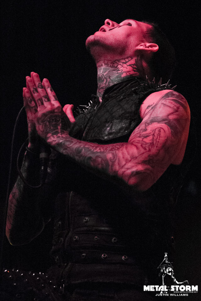 Scott Lewis showing his neck and arm tattoos under stage lights
