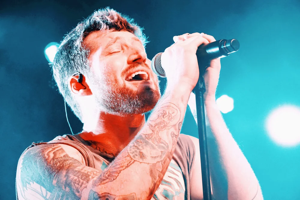 Scotty Sire tattoos: Tattoo evidence: distinct close concert photograph showing the forearm and upper-arm work under colored light.