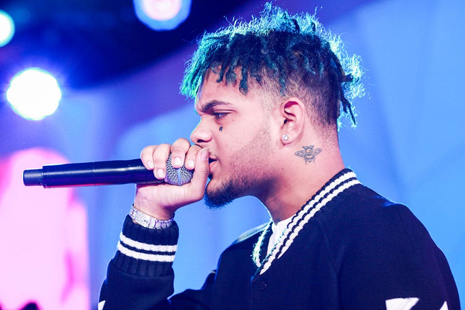 Smokepurpp tattoos: high-resolution stage profile showing the face and neck tattoos under colored lights