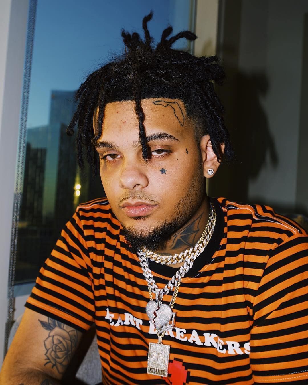 Smokepurpp tattoos: high-resolution portrait showing the face and neck tattoos beside a city window