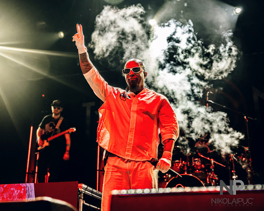 Tech N9ne tattoos: large concert portrait showing the raised tattooed forearm and face-visible performance look