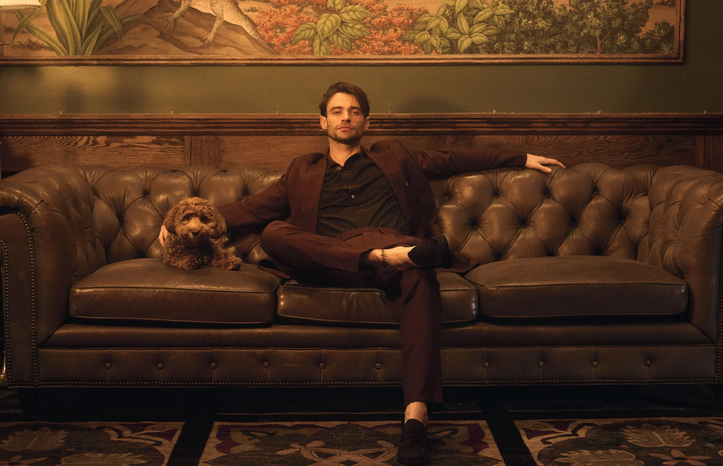 Thomas Doherty tattoos: Thomas Doherty seated portrait with a small lower-leg tattoo visible near the ankle