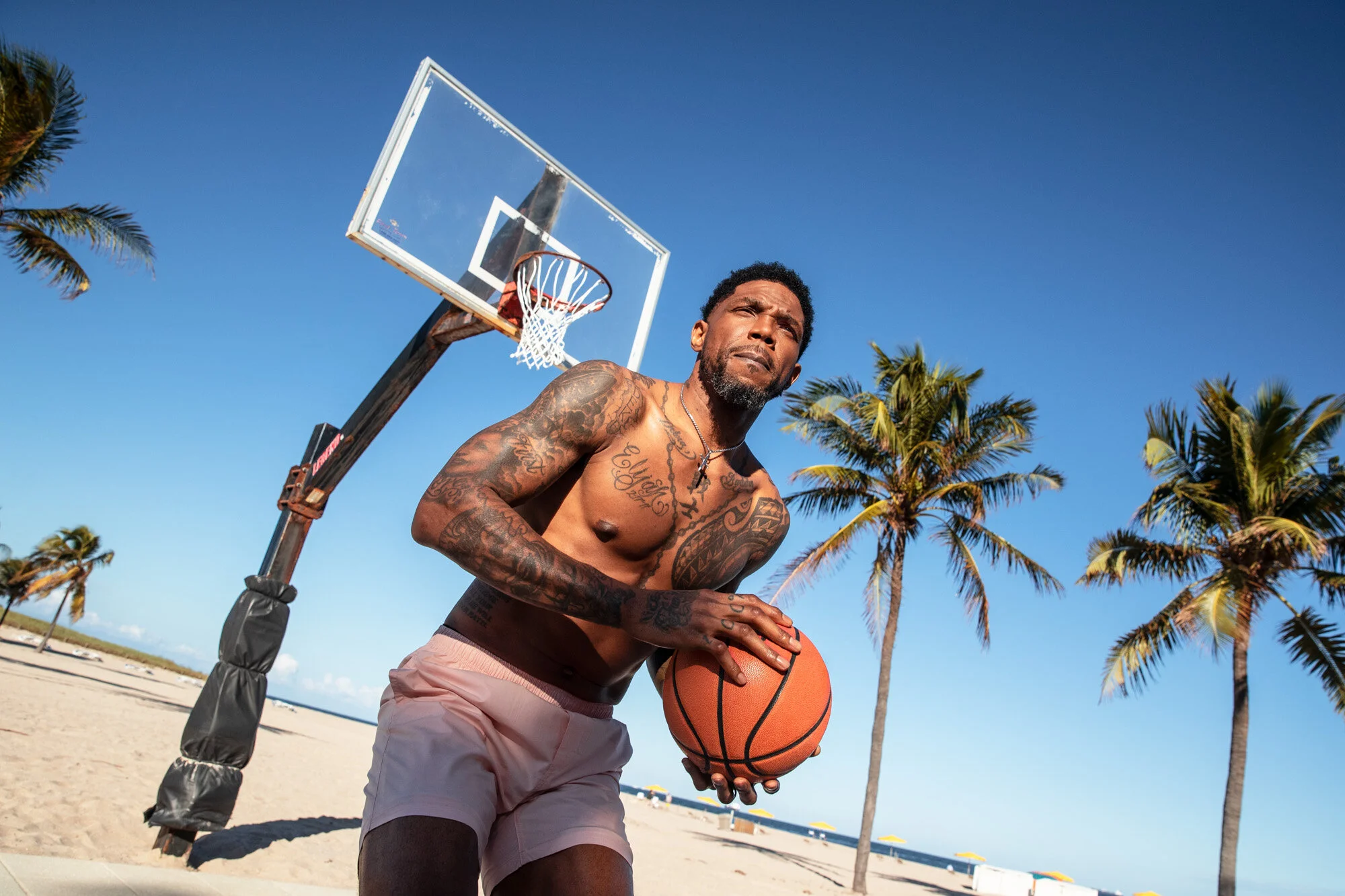 Udonis Haslem tattoos: shirtless beach portrait showing the chest writing, shoulder coverage and forearm ink clearly