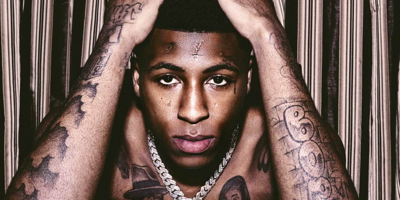 YoungBoy Never Broke Again tattoos: high-resolution portrait showing raised-arm tattoos, facial ink and chest lettering