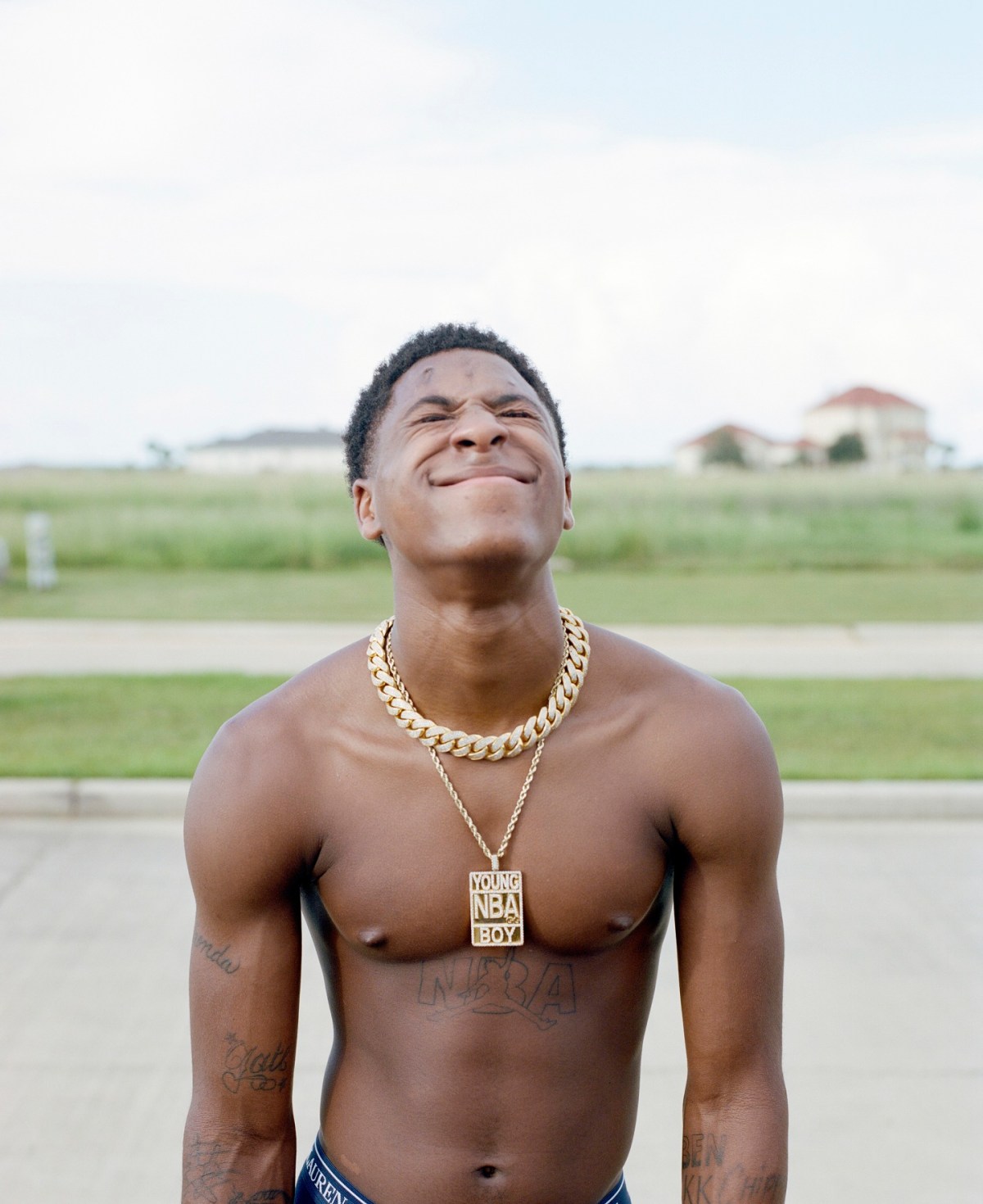 YoungBoy Never Broke Again tattoos: high-resolution outdoor portrait showing chest lettering, arm work and the Young NBA Boy pendant